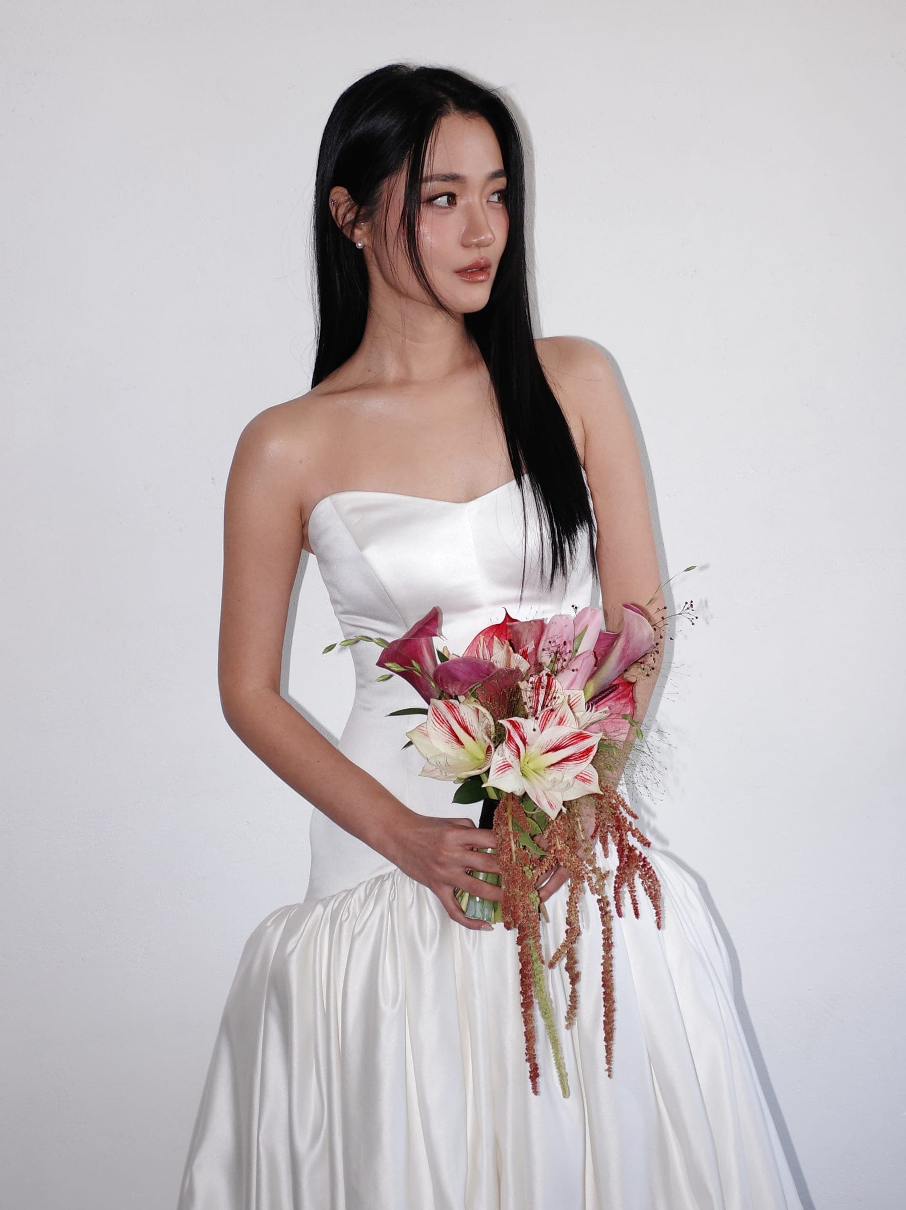 Chaewon holding a bouquet of lilies and calla lilies against a white wall