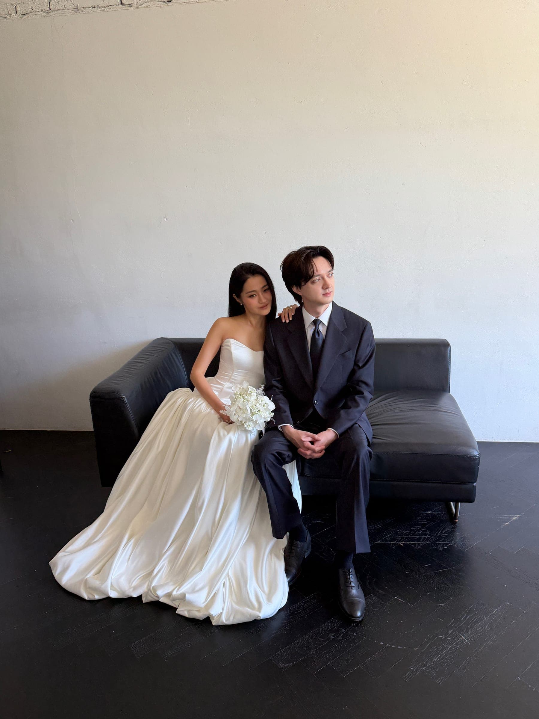 Chaewon and Brandon seated together on a black leather sofa